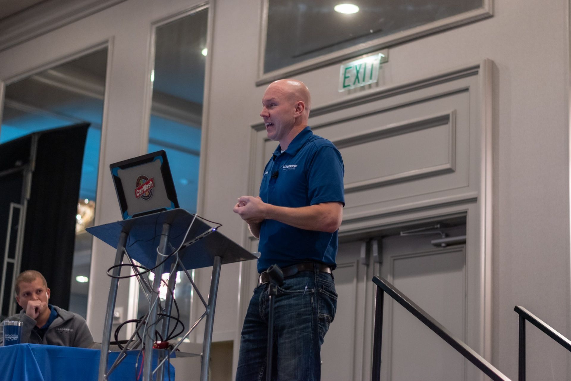 A man is giving a presentation in front of an exit sign