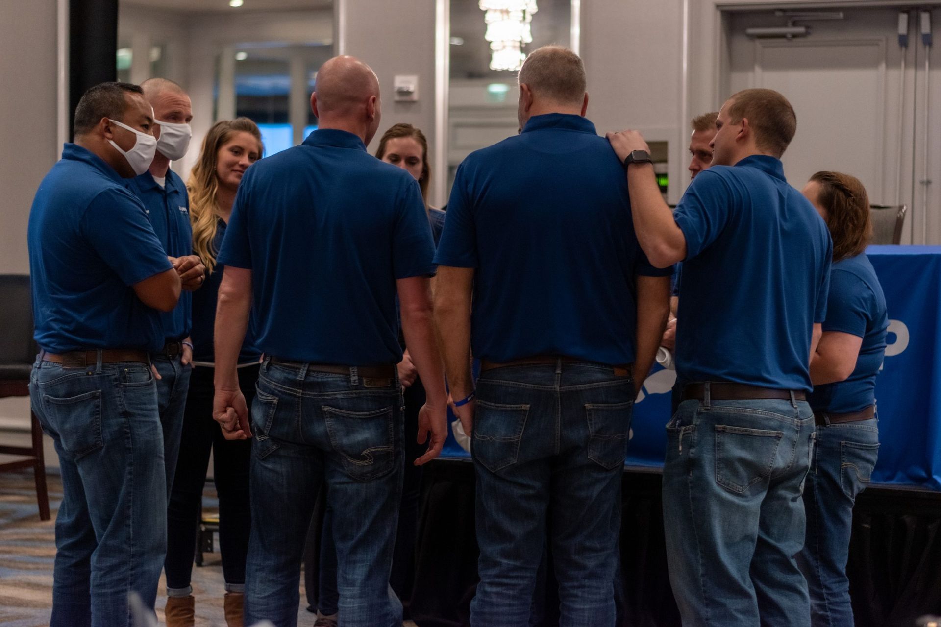 A group of people wearing blue shirts and jeans are standing in a room.