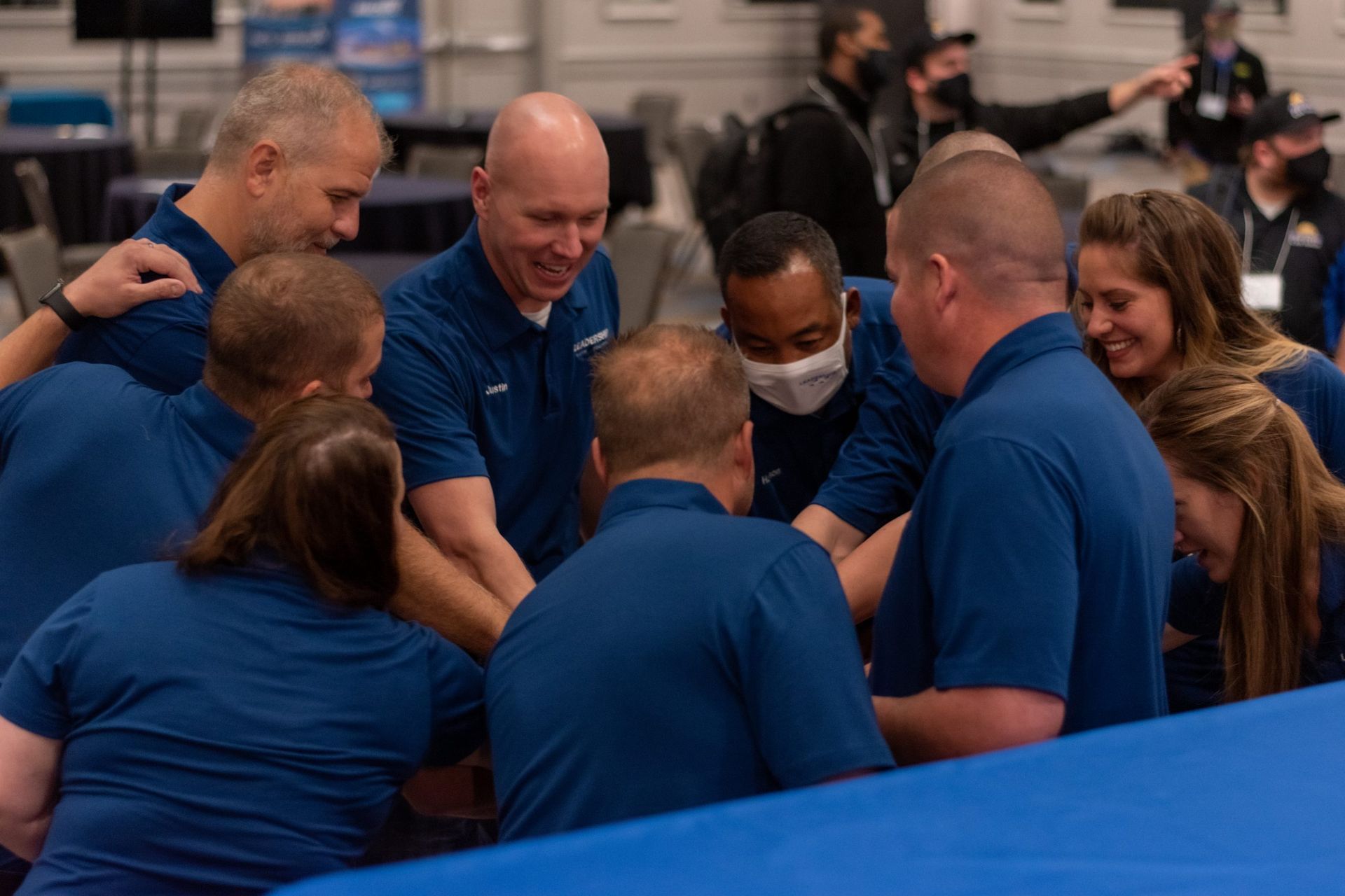 A group of people in blue shirts are huddled together in a room.