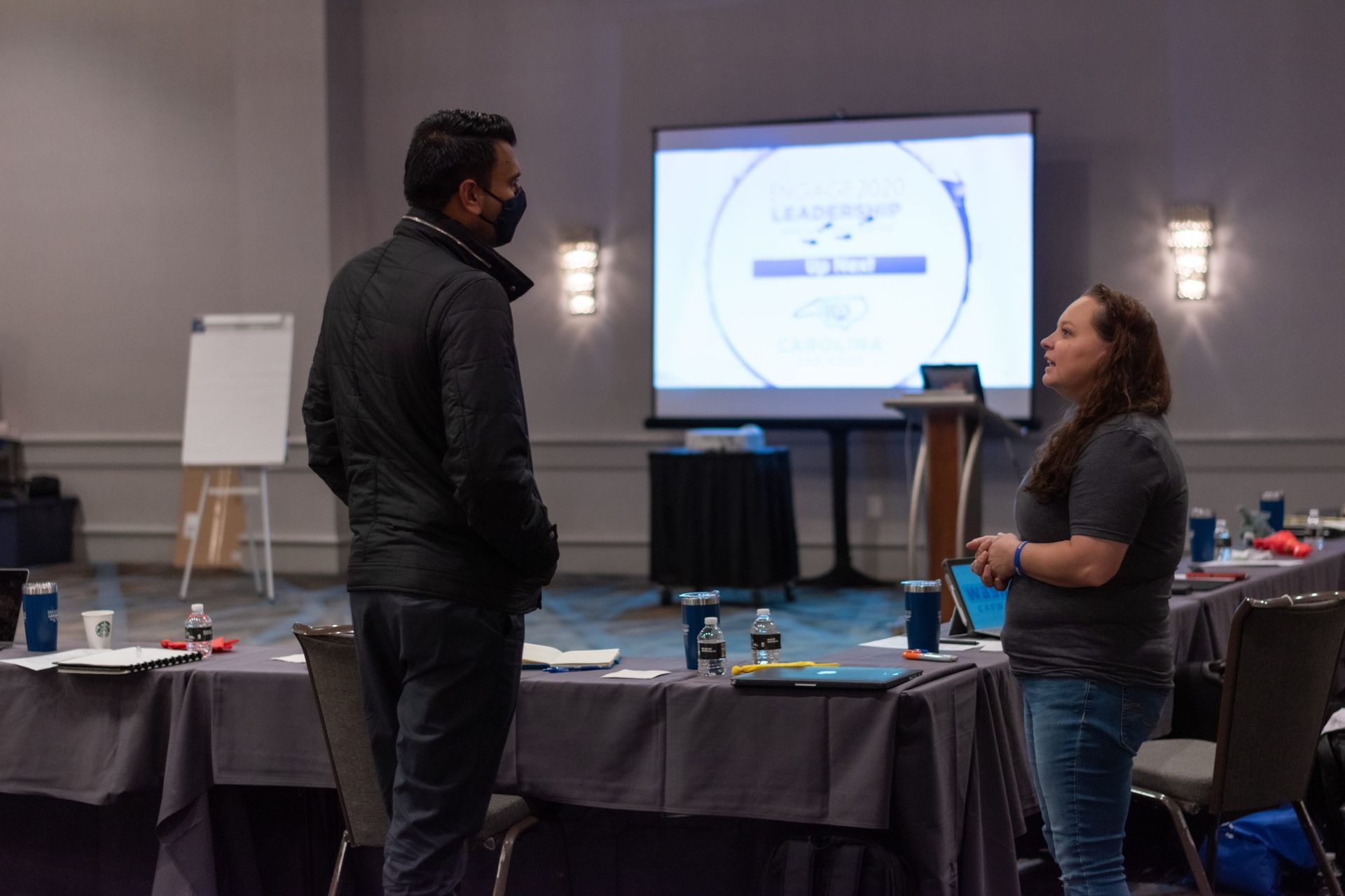 A man and a woman are standing in a conference room talking to each other.