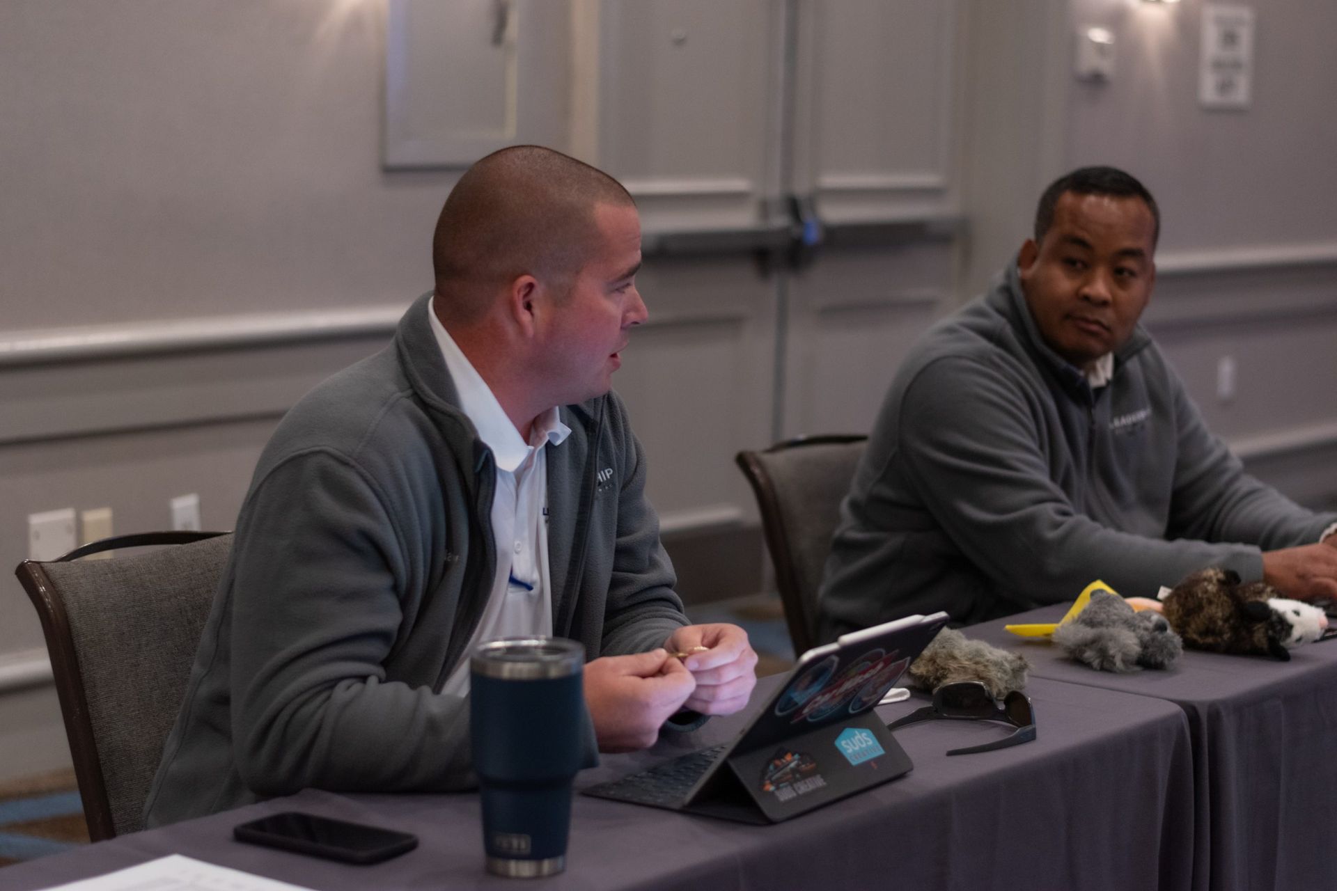 Two men are sitting at a table with a tablet.