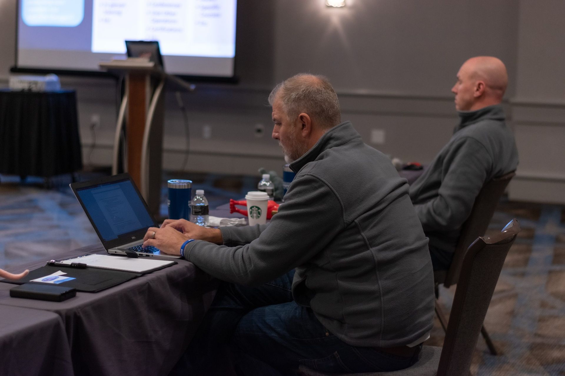 Two men are sitting at a table with laptops in a conference room.