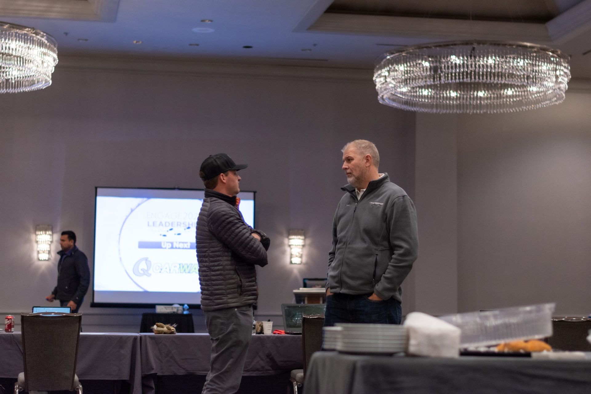 Two men are standing in a room talking to each other.