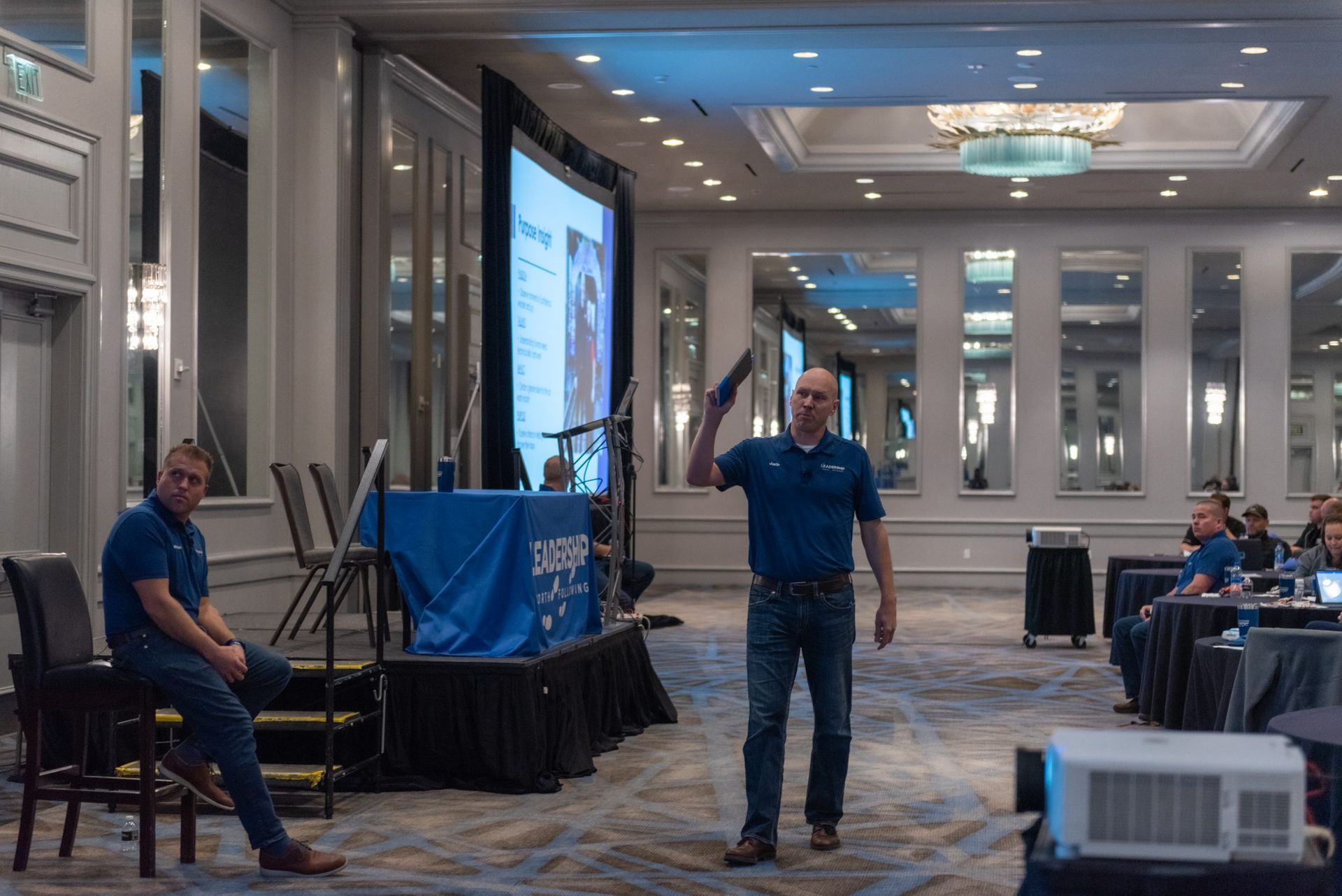 A man is standing in front of a large screen in a conference room.
