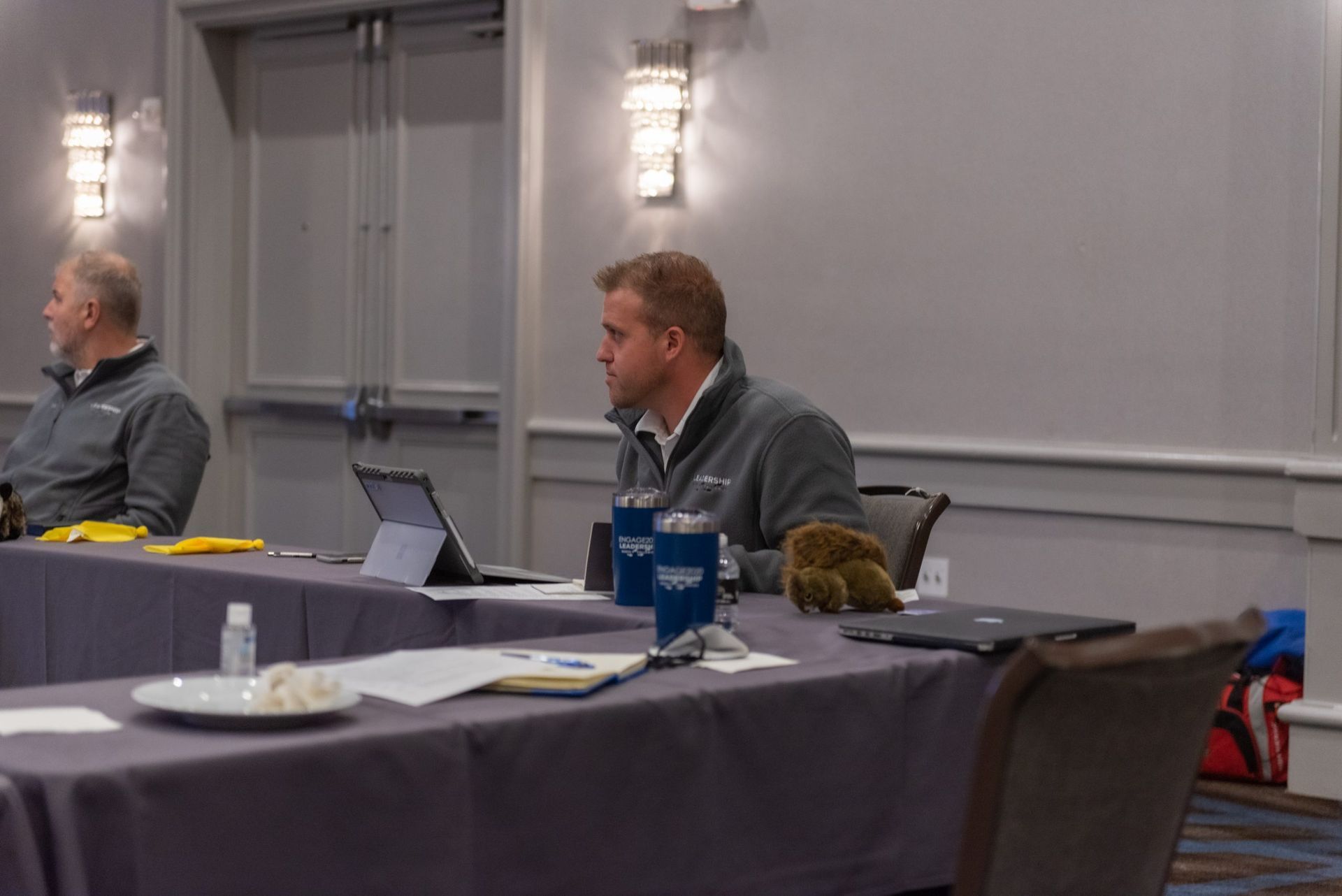 A man is sitting at a table with a laptop in a conference room.