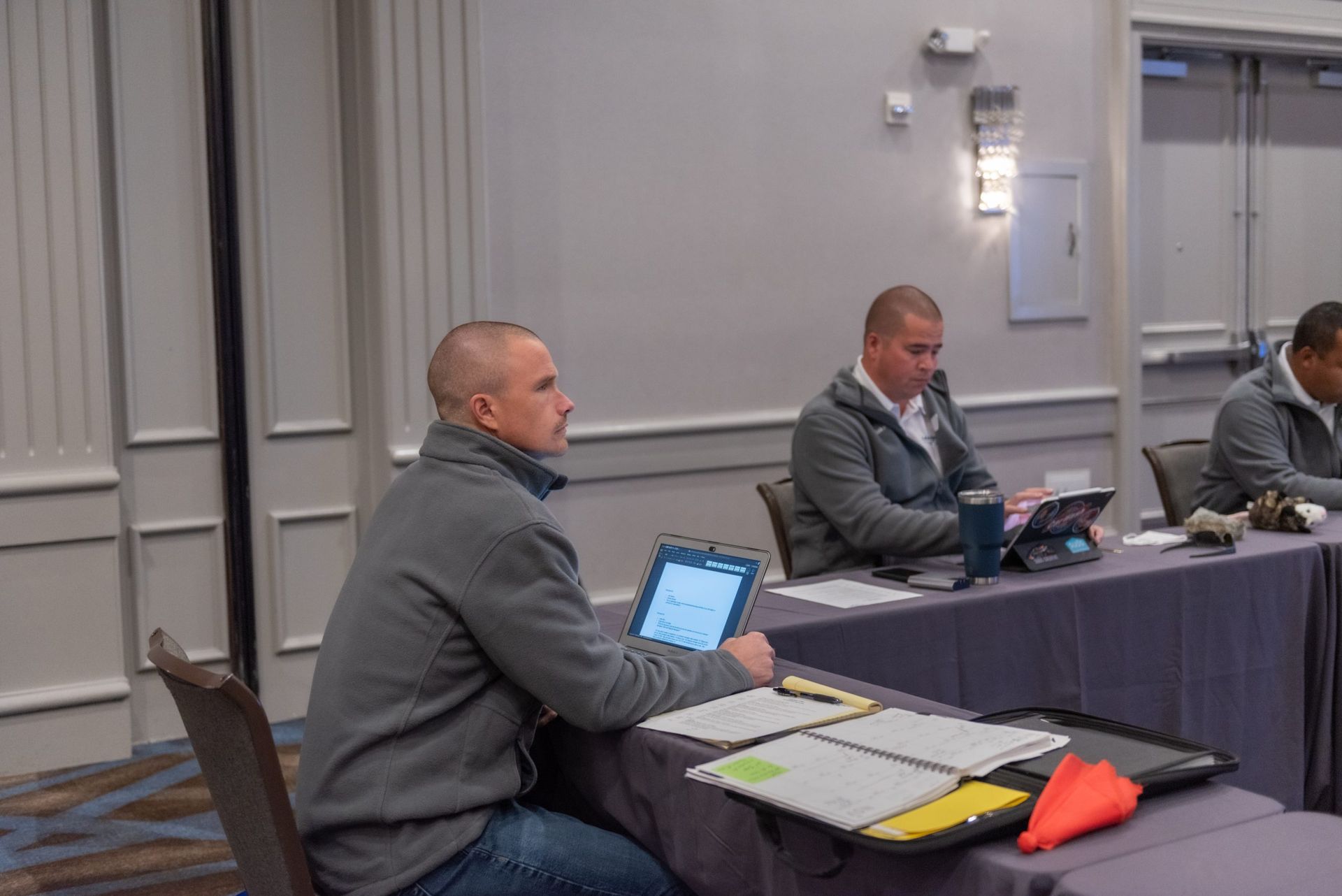 A group of men are sitting at a table with laptops.