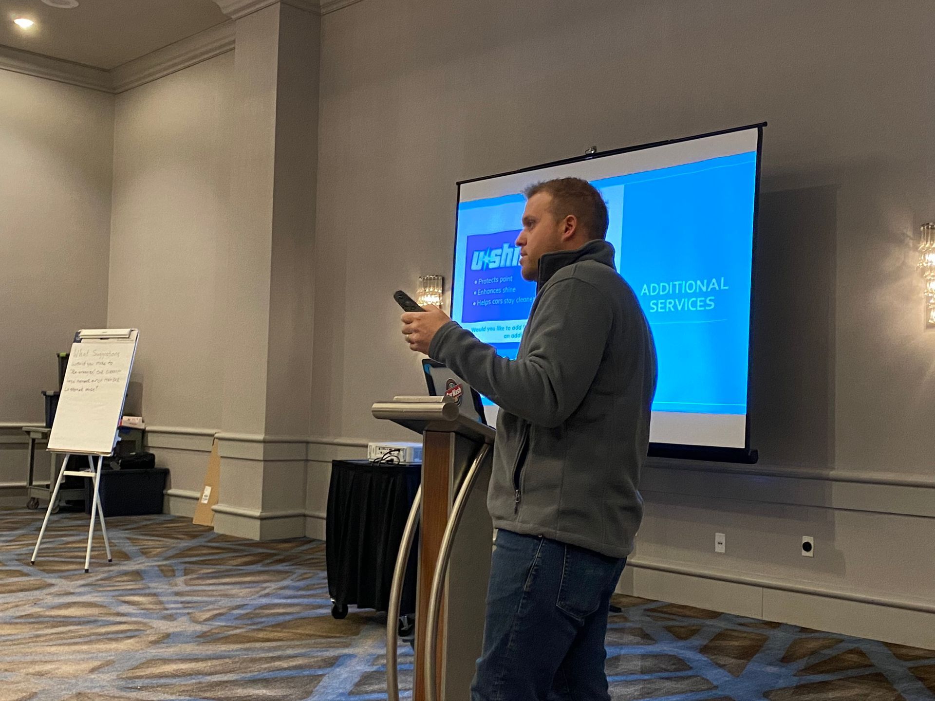 A man is standing at a podium giving a presentation in front of a large screen.