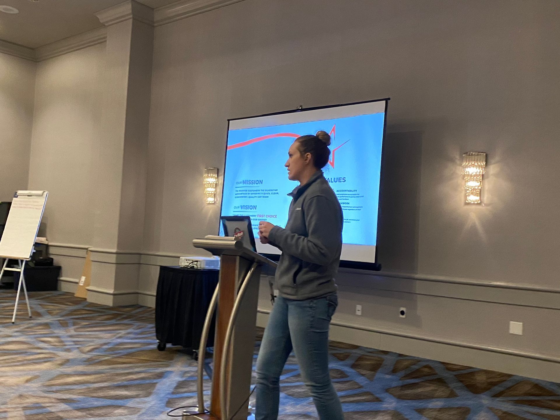 A woman is standing at a podium giving a presentation in front of a large screen.