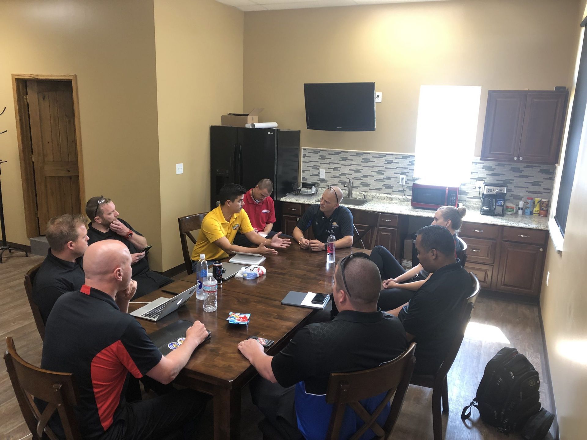A group of men are sitting around a table in a kitchen having a meeting.