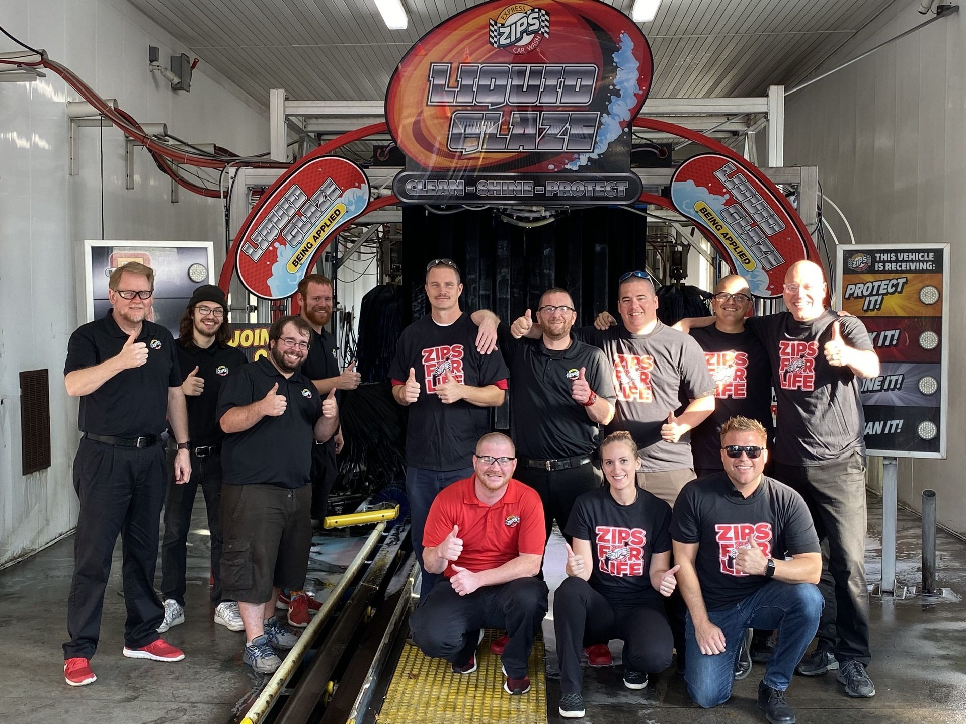 A group of people posing for a picture in front of a car wash machine