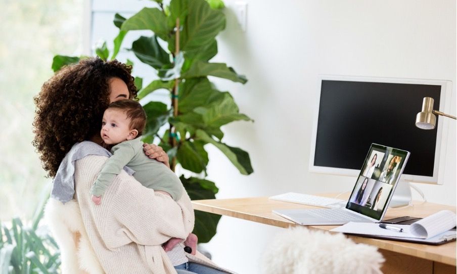 A woman is holding a baby while sitting at a desk in front of a computer.