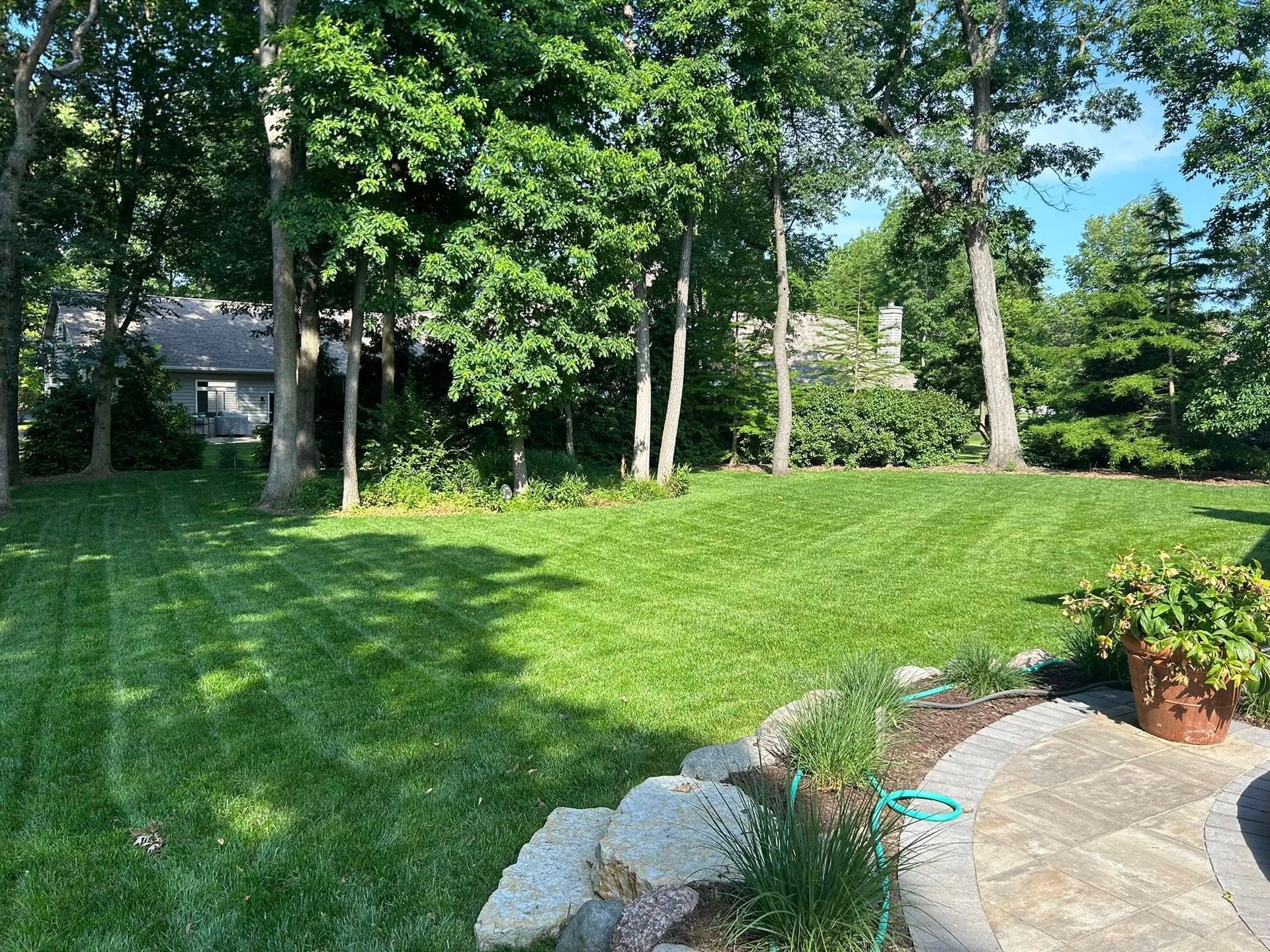 A lush green lawn with trees in the background and a patio in the foreground.
