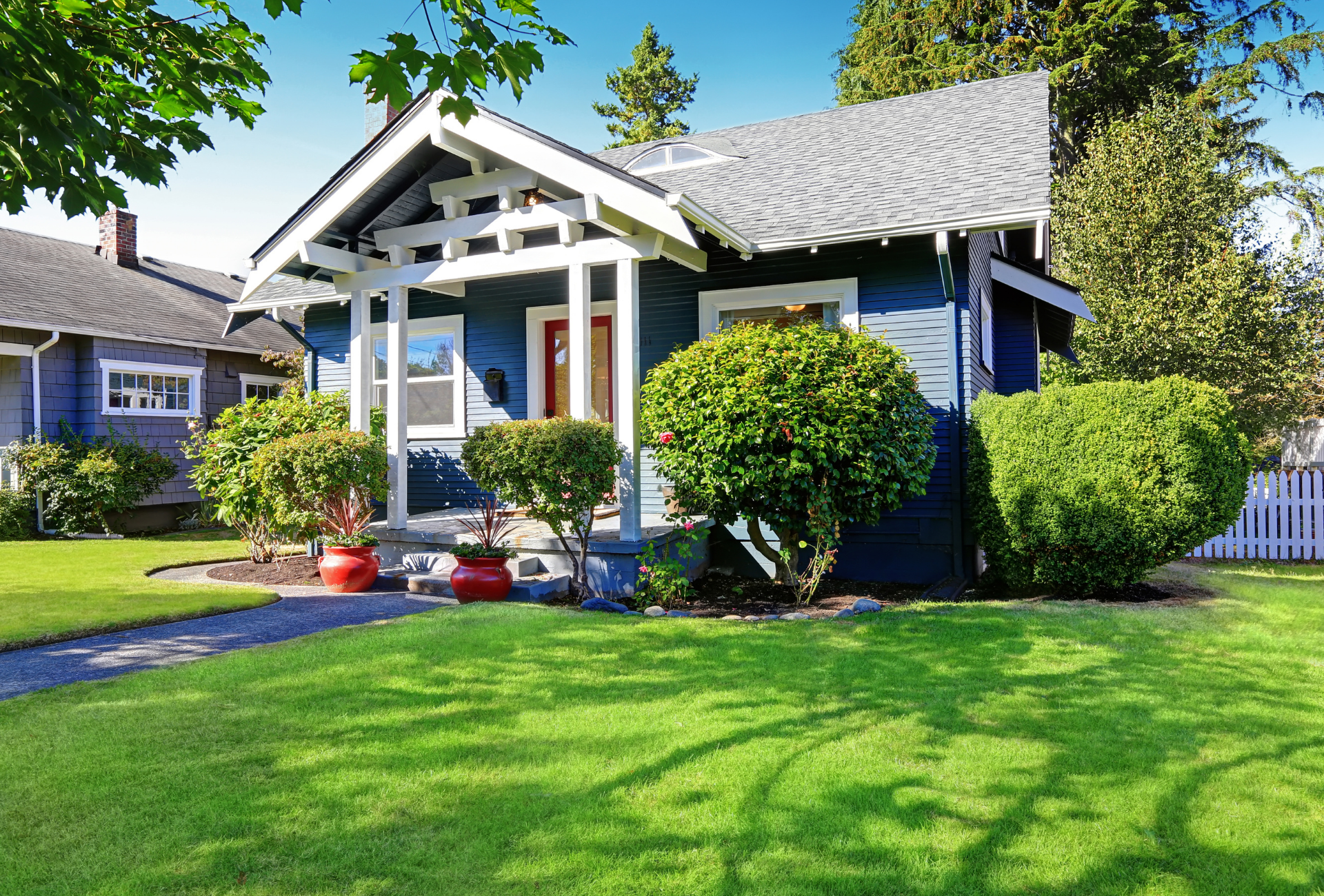 A blue house with a white porch and a lush green lawn in front of it.