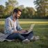 Man using a laptop while sitting on a blanket in a park.
