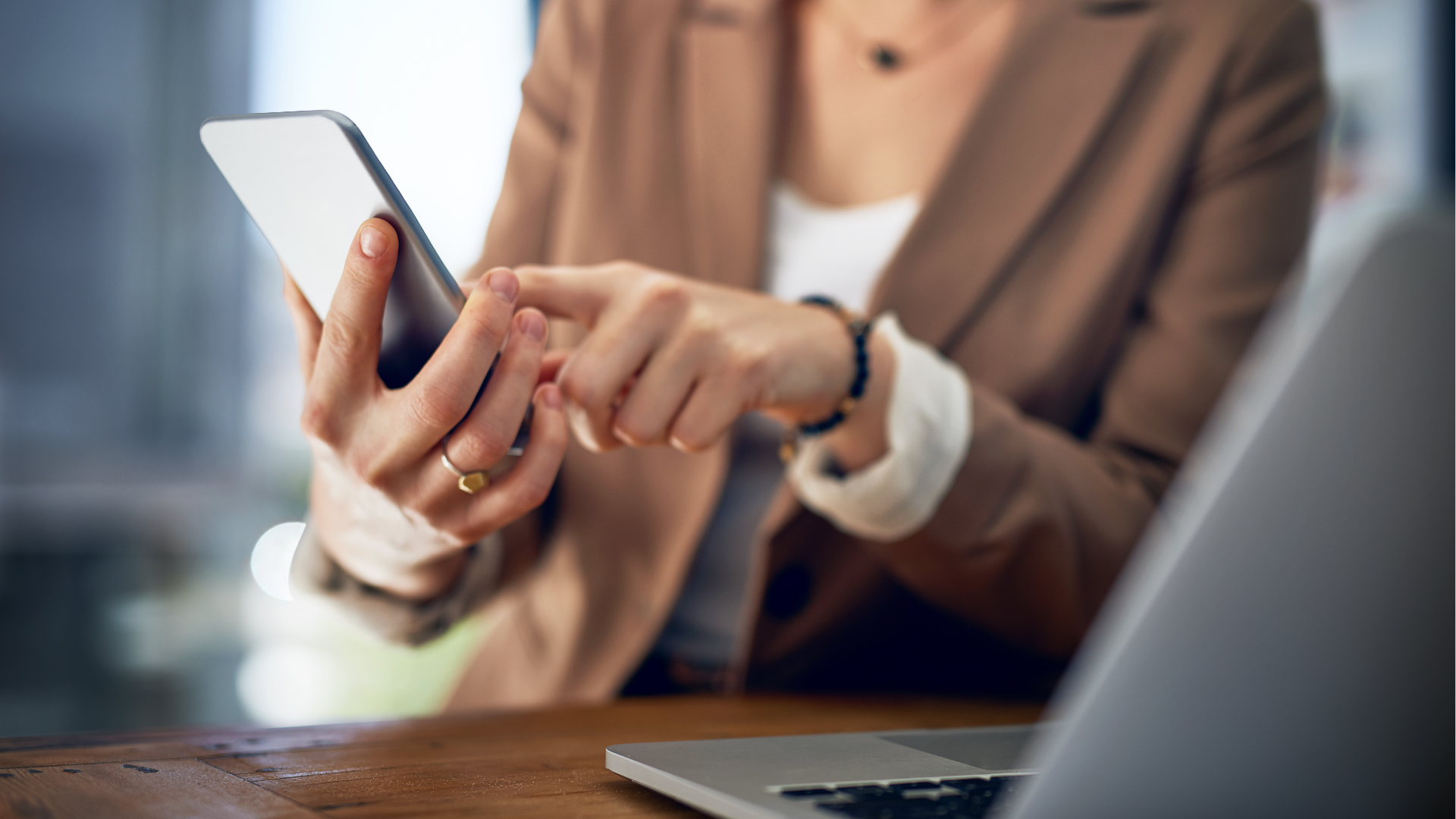 Person typing on laptop, viewing financial charts and pie chart. Phone rests beside the laptop on wooden table.