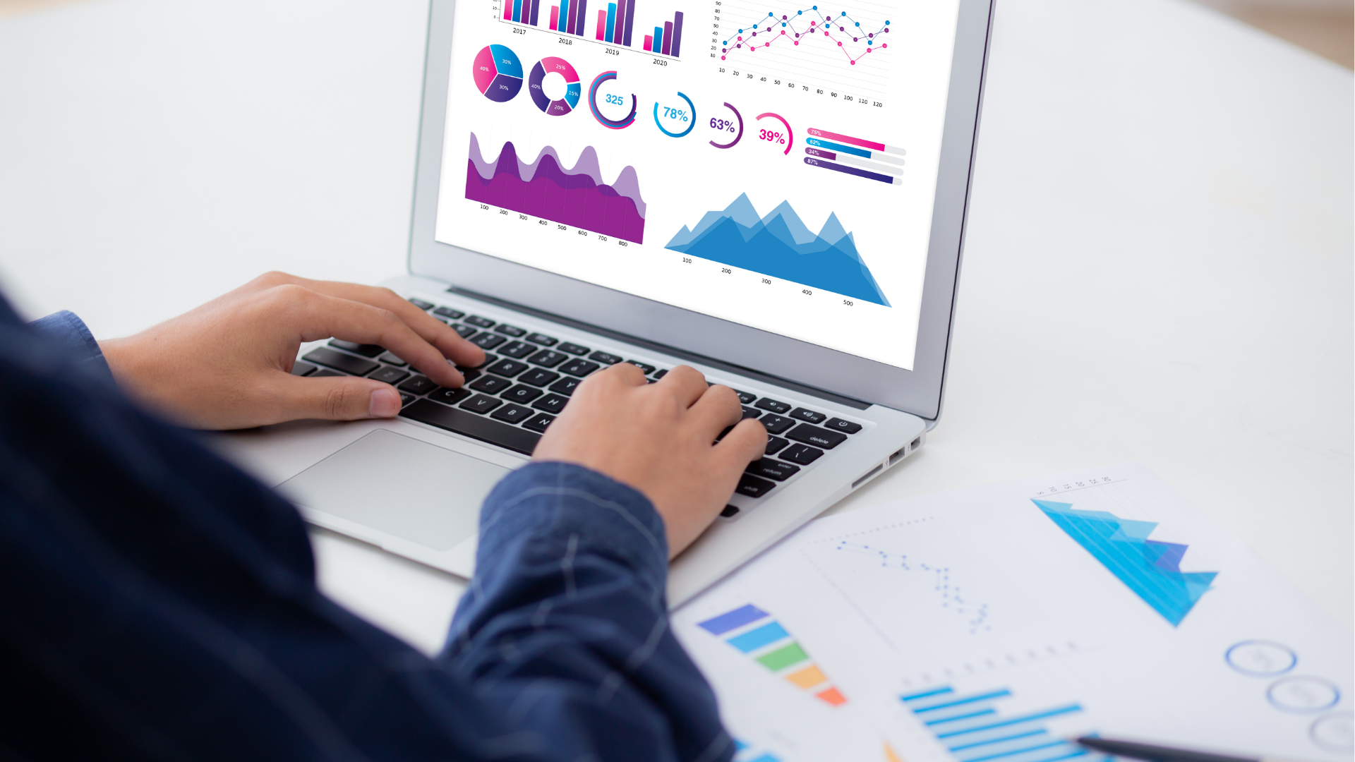 Man with glasses, working on a laptop at a desk with a coffee mug and papers.