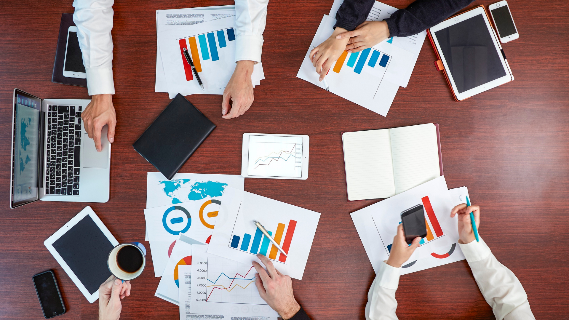 Person typing on laptop, viewing financial charts and pie chart. Phone rests beside the laptop on wooden table.