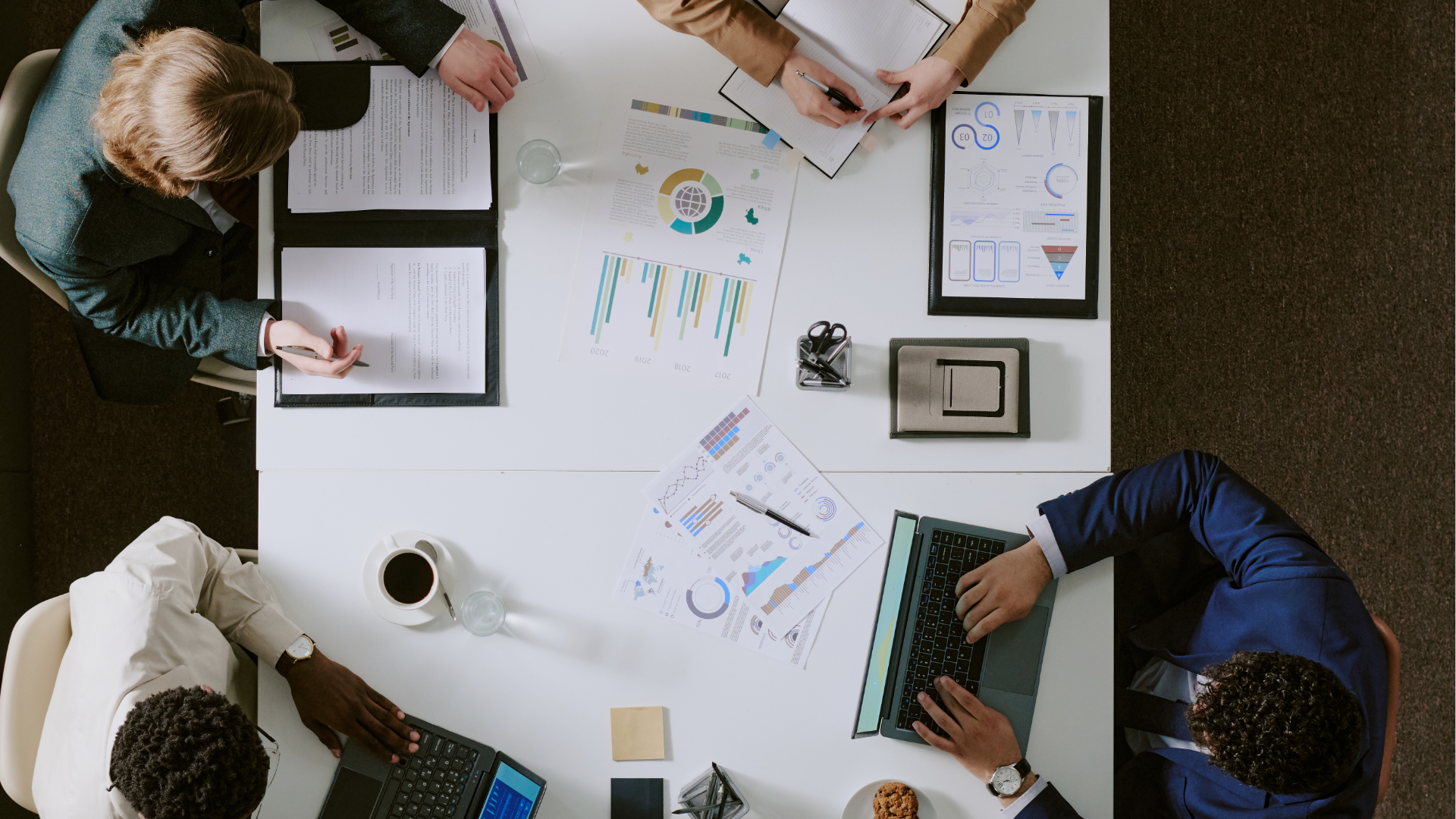 Man with glasses, working on a laptop at a desk with a coffee mug and papers.