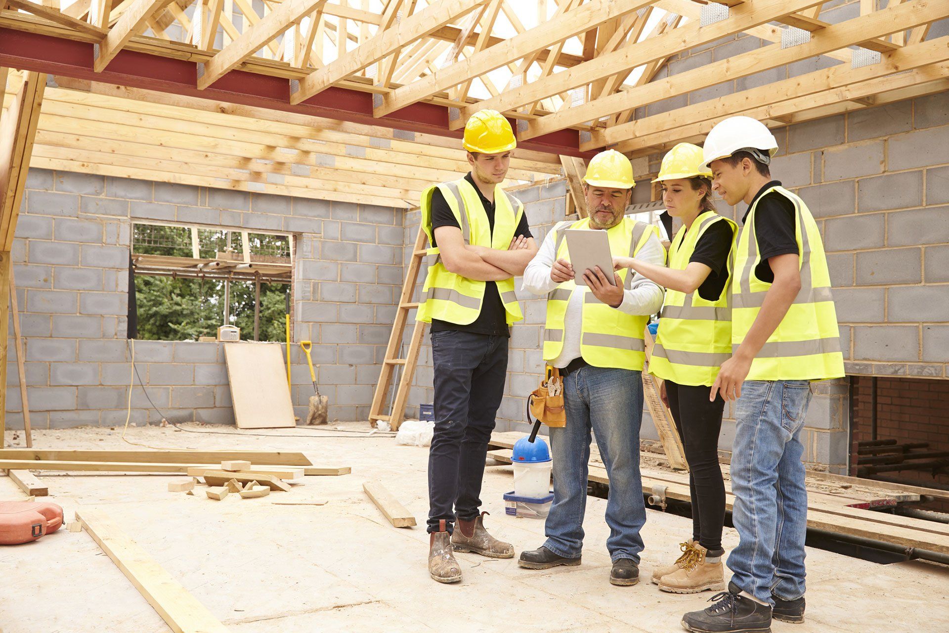 a group of construction workers are standing in a building under construction looking at a tablet .