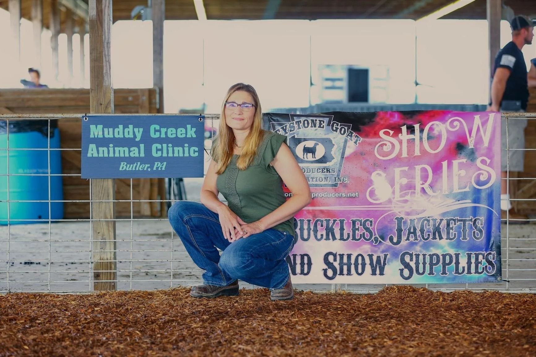 a woman is kneeling in front of a sign that says muddy creek animal clinic