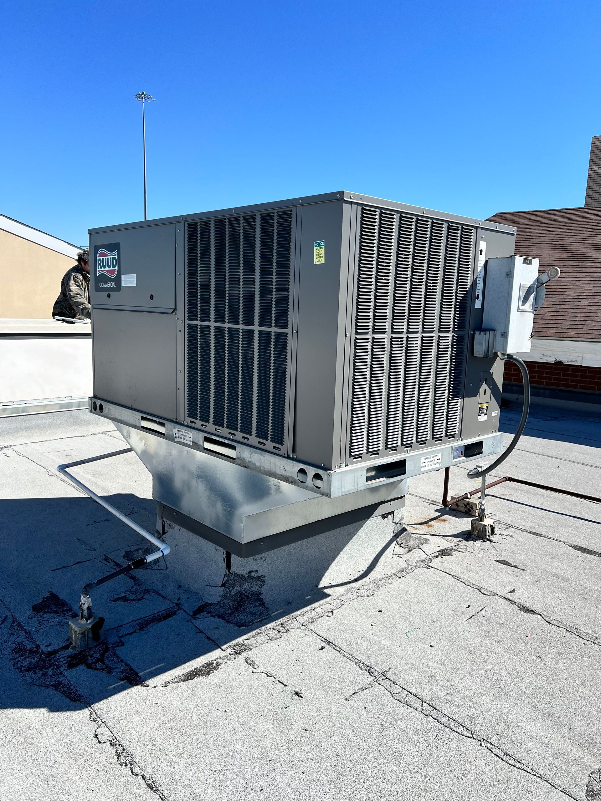 Rooftop with numerous air conditioning units, rectangular building, and small white structure.