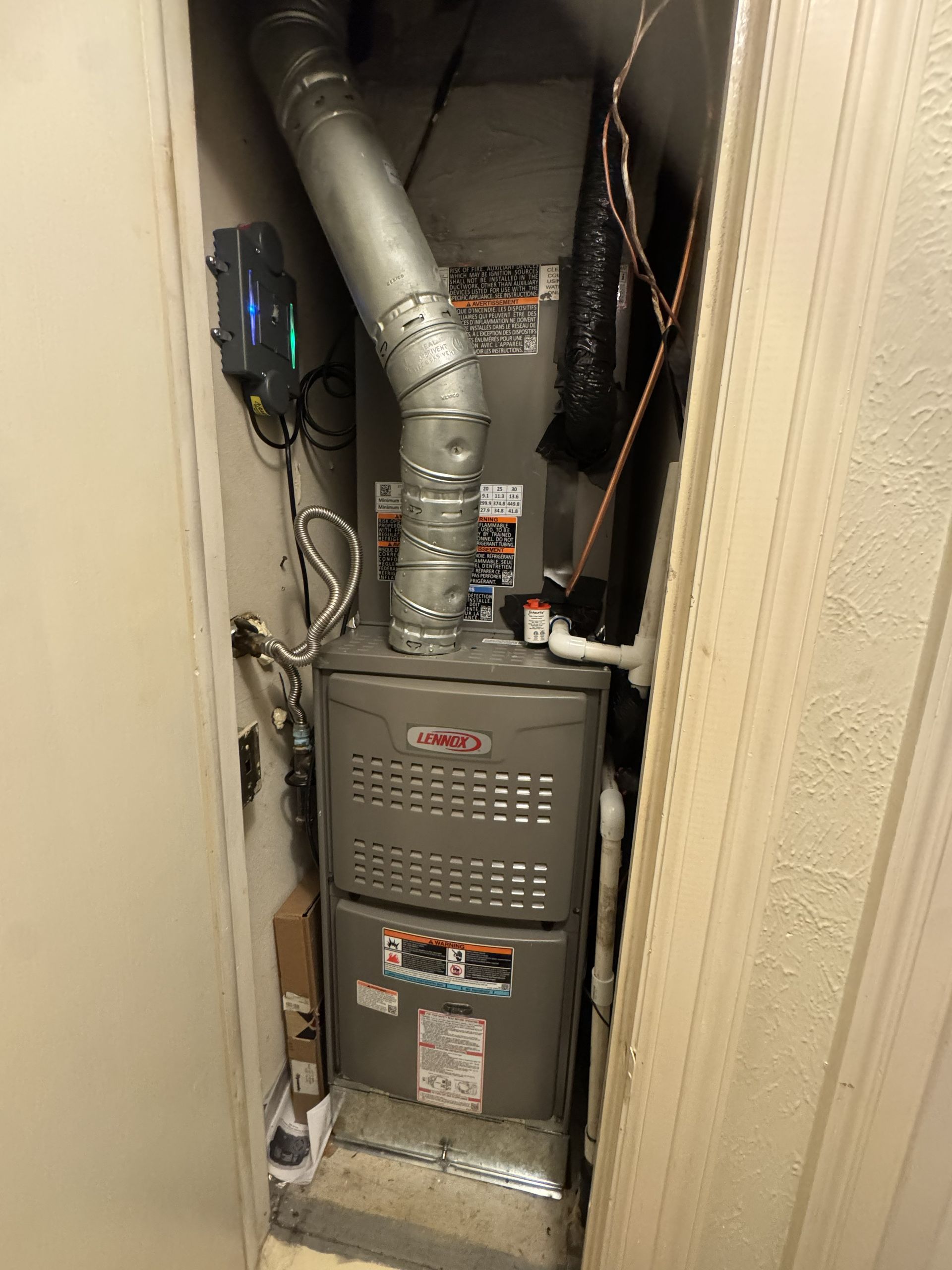 Furnace unit inside a closet with ductwork and connected wires.