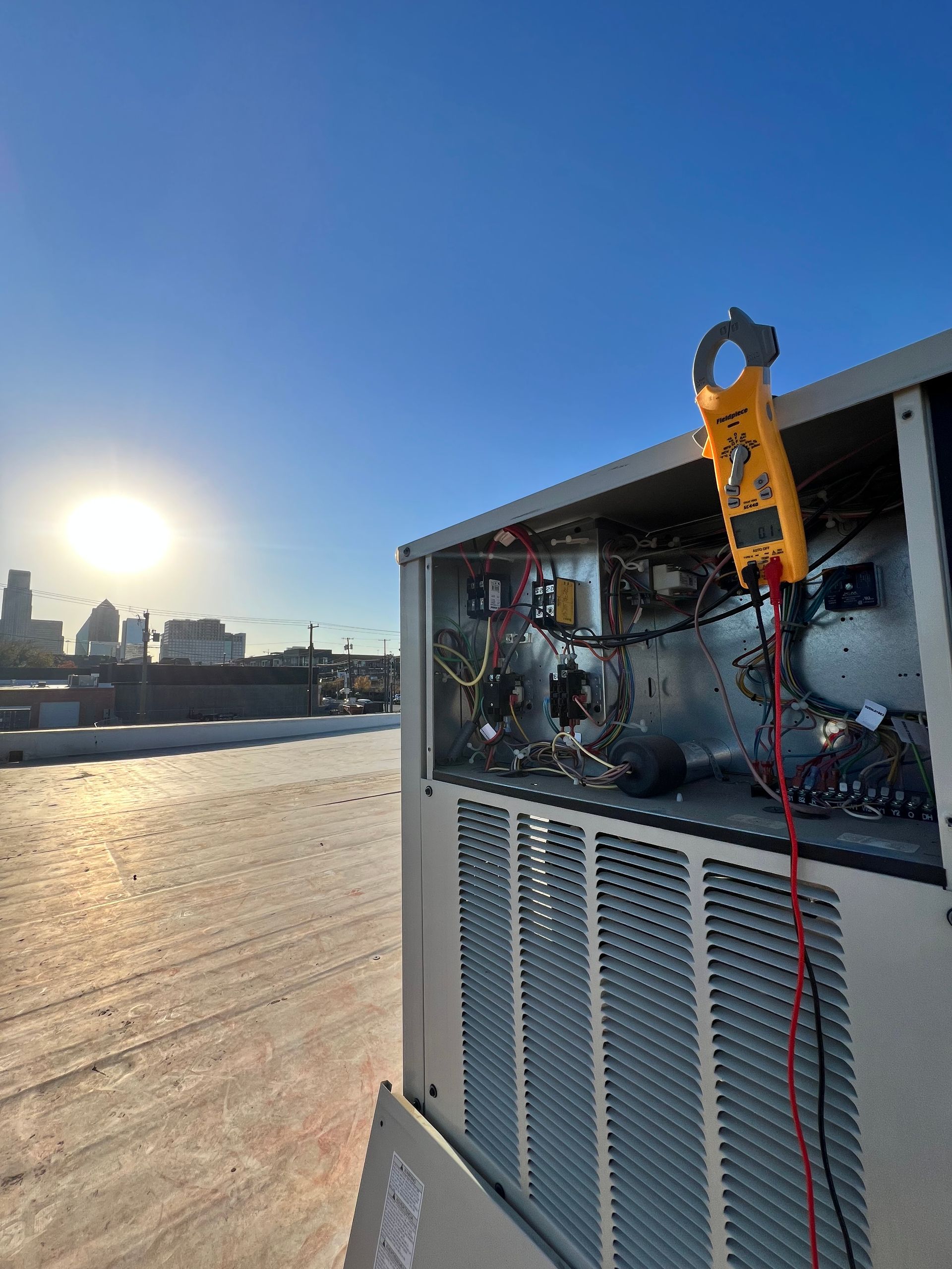 HVAC technician working on rooftop air conditioning unit under a blue sky.