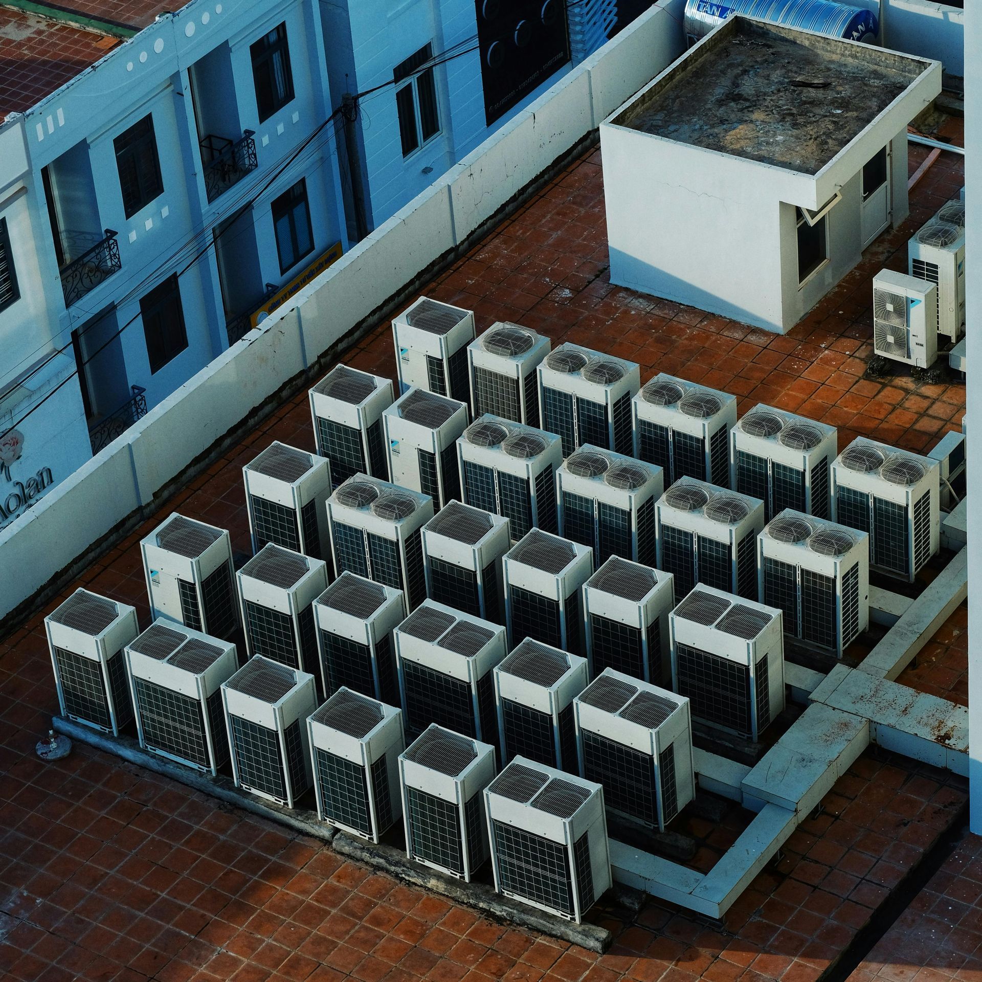 Rooftop with numerous air conditioning units, rectangular building, and small white structure.
