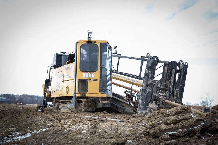 Yellow trencher digging a trench in a muddy field under an overcast sky.