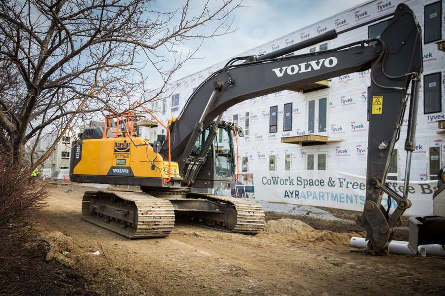 Yellow and black Volvo excavator at a construction site, near a partially built apartment building.