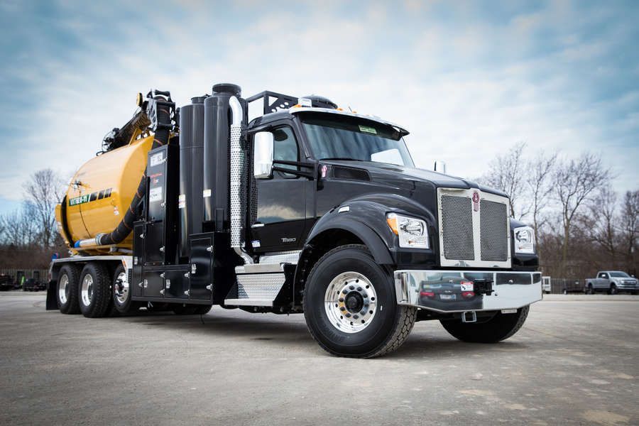 Black Kenworth vacuum truck parked in a paved lot on a cloudy day. The truck has a yellow tank and silver accents.
