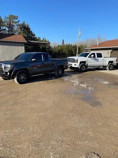 Two trucks are parked in a dirt lot in front of a house.