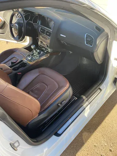The interior of a white car with brown seats and a steering wheel.