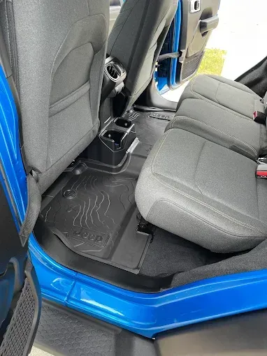 The back seat of a blue jeep wrangler with the door open.