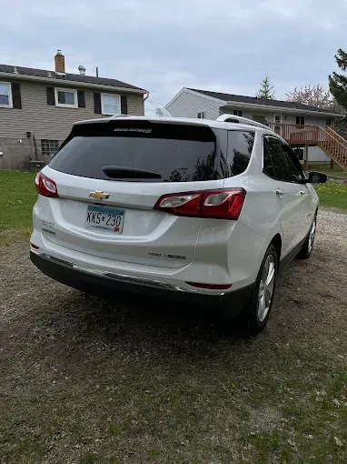 A white chevrolet equinox is parked in a driveway in front of a house.