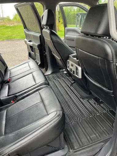 The back seat of a car with black leather seats and a mat.