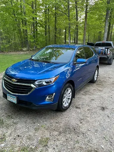 A blue car is parked on a dirt road next to a truck.