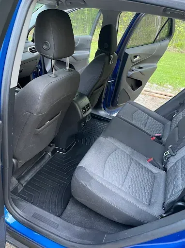 The back seat of a blue car with black seat mats.