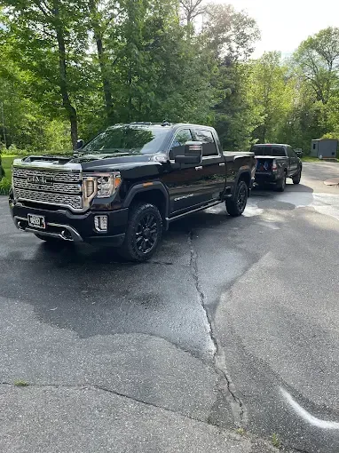 A black truck is parked on the side of the road next to another truck.