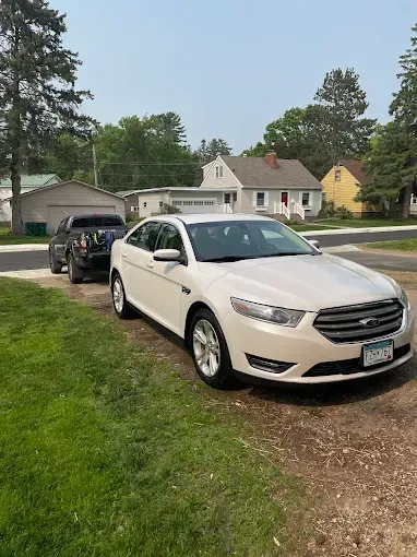 A white car is parked in a grassy area next to a black truck.