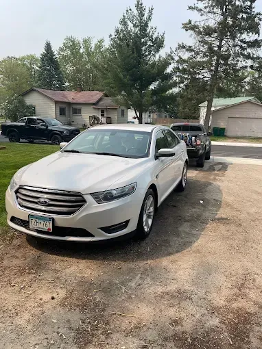 A white ford taurus is parked in a driveway next to a black truck.