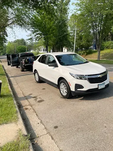 A white car is parked on the side of the road next to a truck.