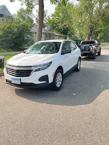 A white car is parked on the side of the road next to a truck.