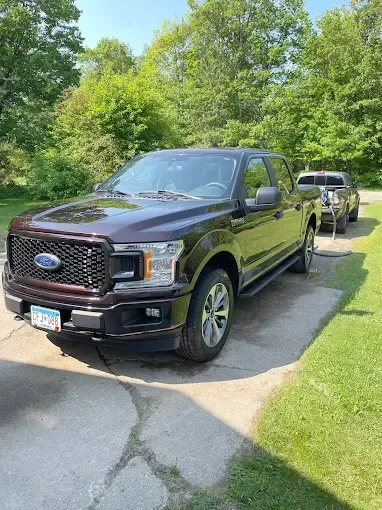 A black ford f150 truck is parked in a driveway next to another truck.