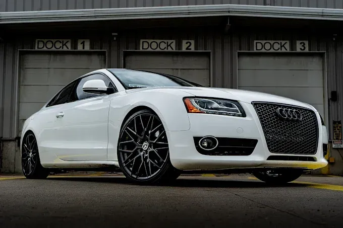 A white audi a5 coupe is parked in front of a garage door.