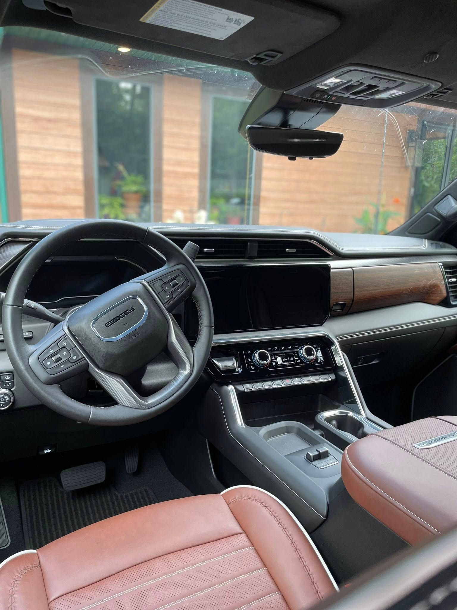 Interior of a GMC Yukon, brown leather seats, dark dashboard, steering wheel, and exterior view.