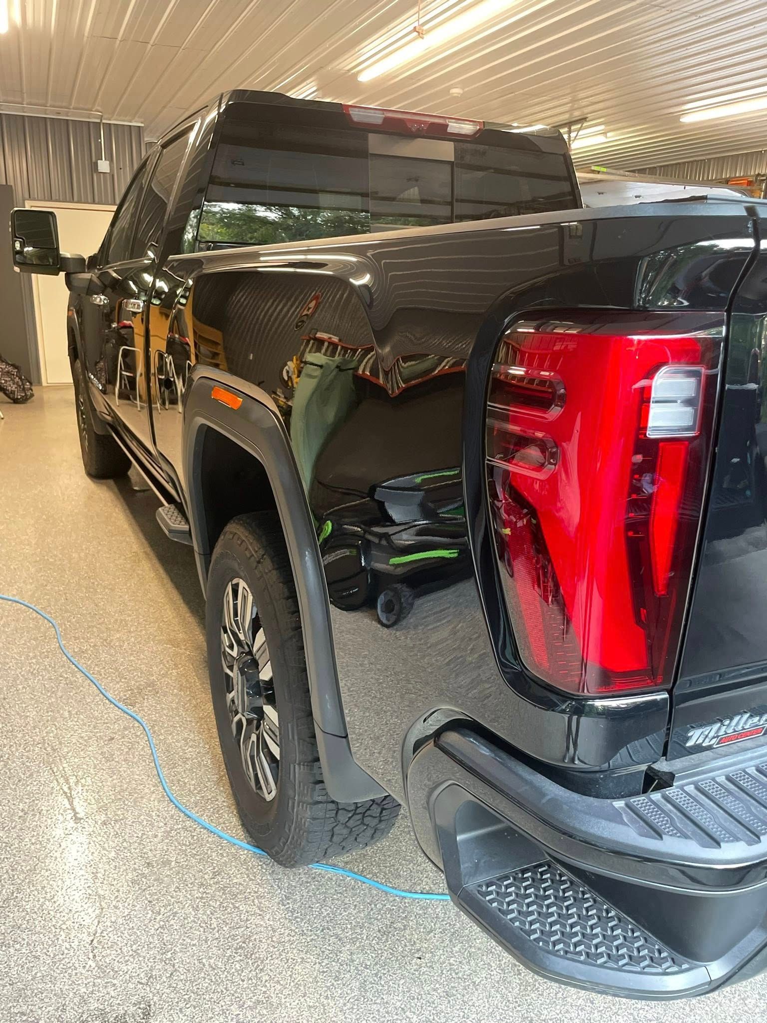 Black GMC truck parked indoors with reflections, red taillight, and side steps.