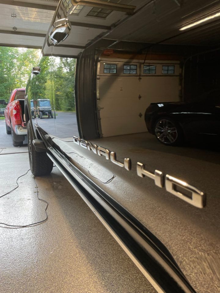 Ceramic Coating Detail on Denali HD truck emblem next to a side step on a garage floor, with a truck and garage door in the background.