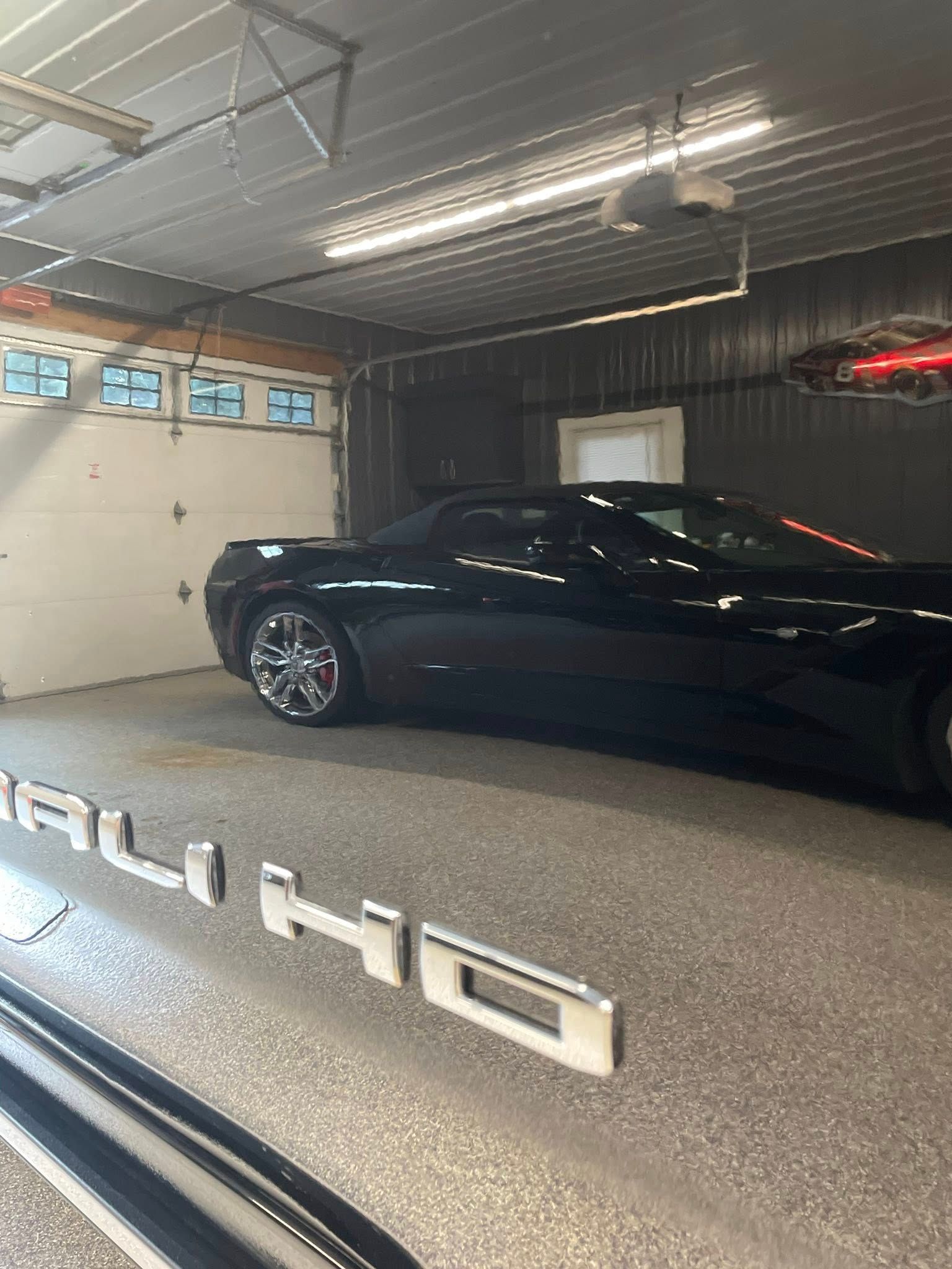 Black sports car inside a garage. Chrome wheels, shiny floor, overhead lights.