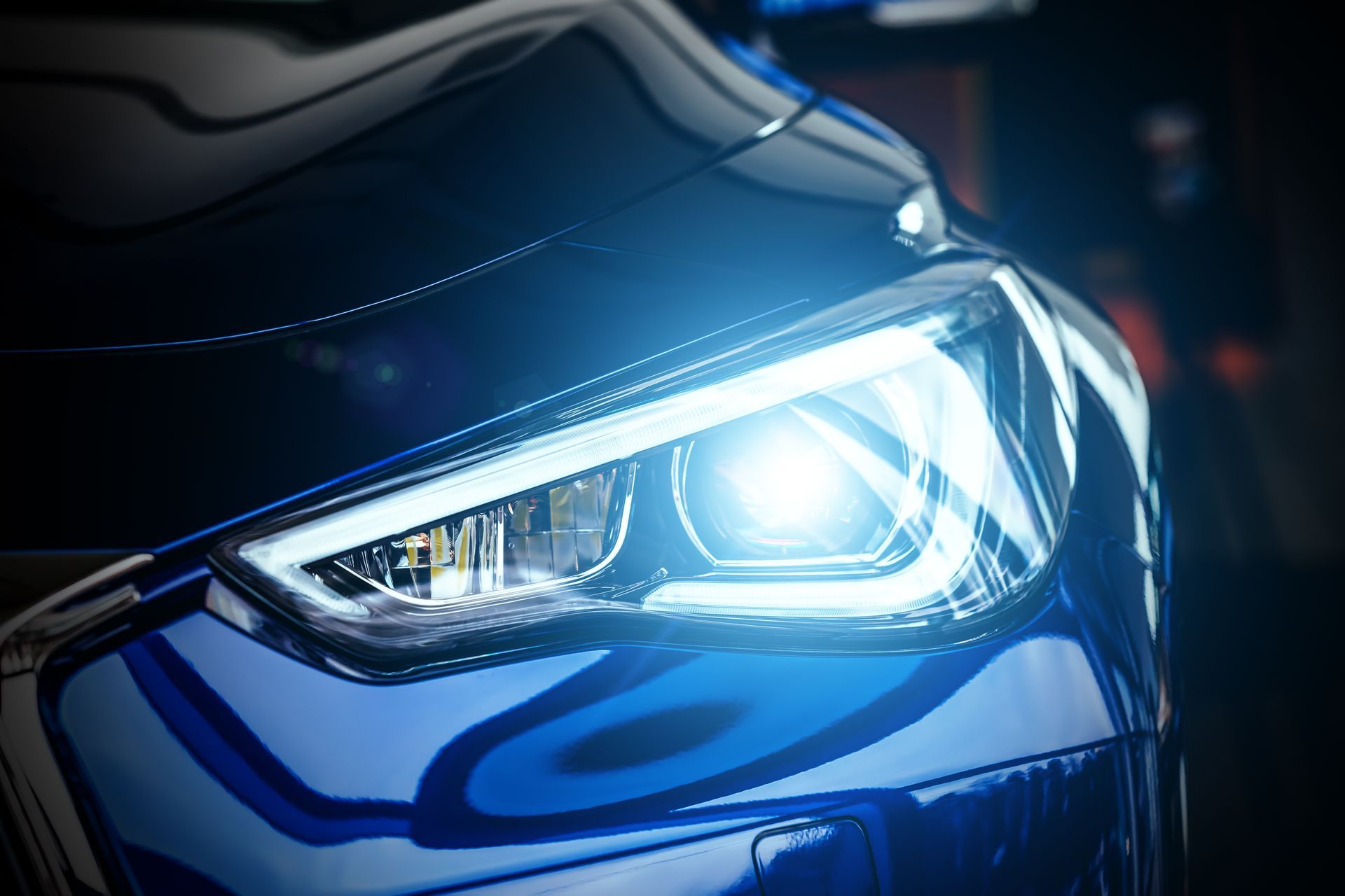 Close-up of a blue car’s illuminated headlight shining brightly in the dark.